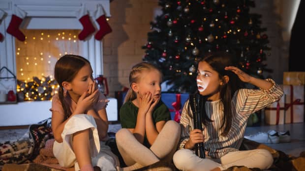 青春期前的女孩手里拿着一个手电筒和害怕说话的朋友与圣诞装饰壁炉附近的一条毯子和一个树在后台。