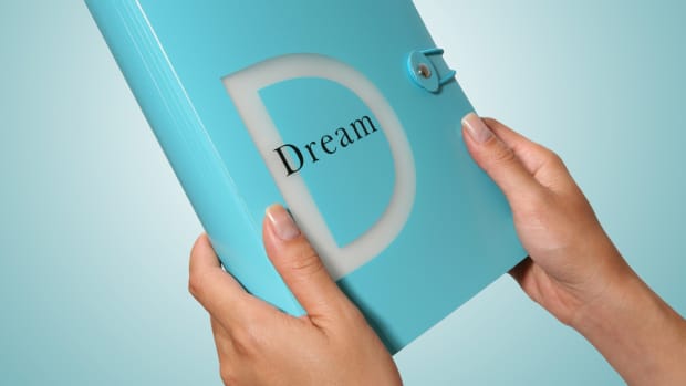 女人的手拿着光teal笔记本用透明字母“D”和“梦想”这个词写在前面。