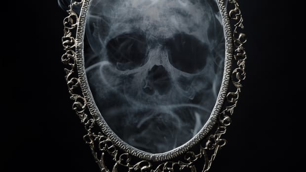 一个幽灵,烟雾缭绕的头骨盘旋在一个华丽的椭圆形的镜子。